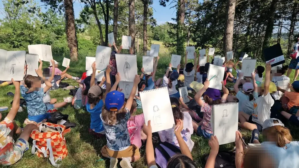 Les élèves de CE2 brandissent leurs carnets de dessin devant la statue d'Alésia