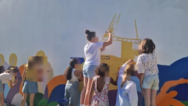 Un groupe d'élèves monte sur un banc pour peindre la partie haute de la fresque